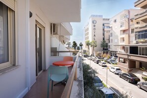 Un balcón con mesa y sillas, con vista a una calle con coches estacionados y un edificio con la leyenda 'ROYAL'.