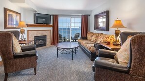 Hotelkamer met een open haard, televisie, bank, twee fauteuils, salontafel en uitzicht op zee door grote ramen.