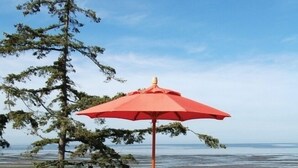 Een terras met een tafel en stoelen, een rode parasol, en uitzicht op de oceaan.