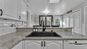 Eine moderne Küche mit weißen Schränken, Granit Arbeitsplatten, einem schwarzen Wasserhahn und einem integrierten Geschirrspüler.