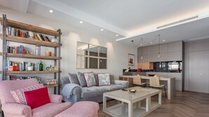 A modern living room with a sofa, ottoman, and coffee table, a bookshelf, and a kitchen area with a dining table and chairs. - Bright & Functional Studio Near Bernabéu (Madrid)