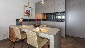 A modern kitchen with a central island, a dining area with wicker chairs, and a large window overlooking the city. - Bright & Functional Studio Near Bernabéu (Madrid)