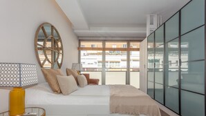 A modern bedroom with a large bed, a round mirror, a glass table, and a view of the city through large windows. - Bright & Functional Studio Near Bernabéu (Madrid)