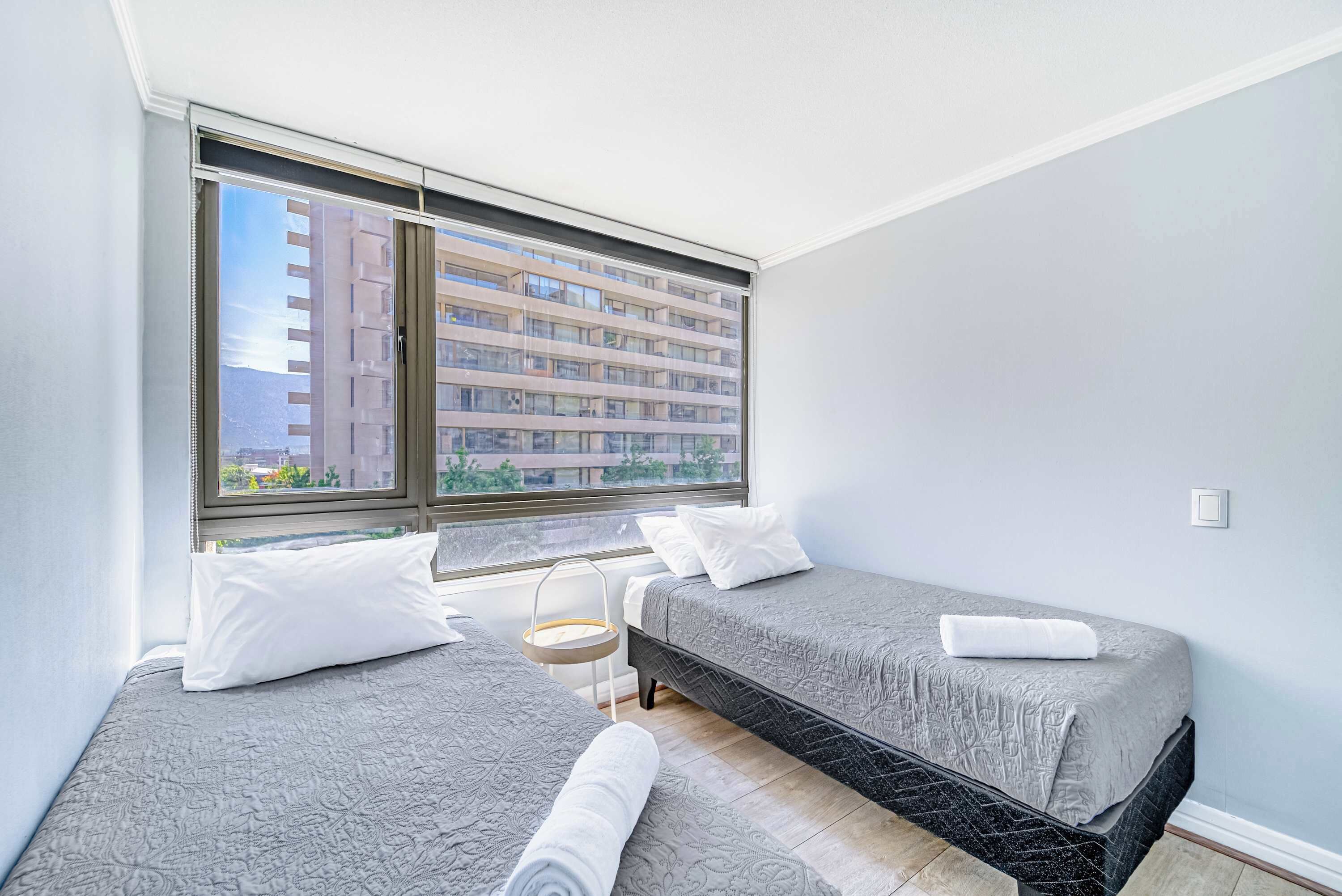 Une chambre avec deux lits, une fenêtre avec des stores et une vue sur un bâtiment à l’extérieur.