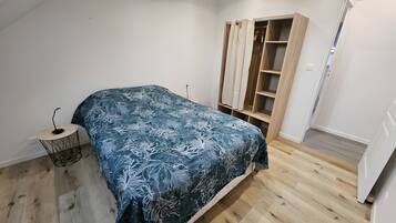 Une chambre à coucher comprenant un lit, une table de chevet, une armoire et un petit tabouret.