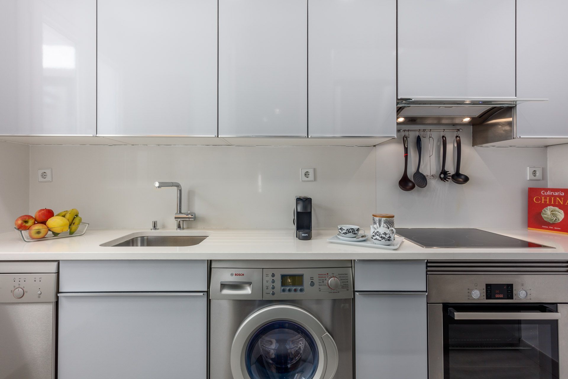 A modern kitchen with a dishwasher, washing machine, and oven.