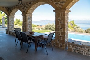 A stone-arched patio with a wooden table and chairs, overlooking a swimming pool and a scenic view of the sea and mountains. - Villa Kalamos/Sea View and Pool nearby Athens/Superior Villa (oropos)