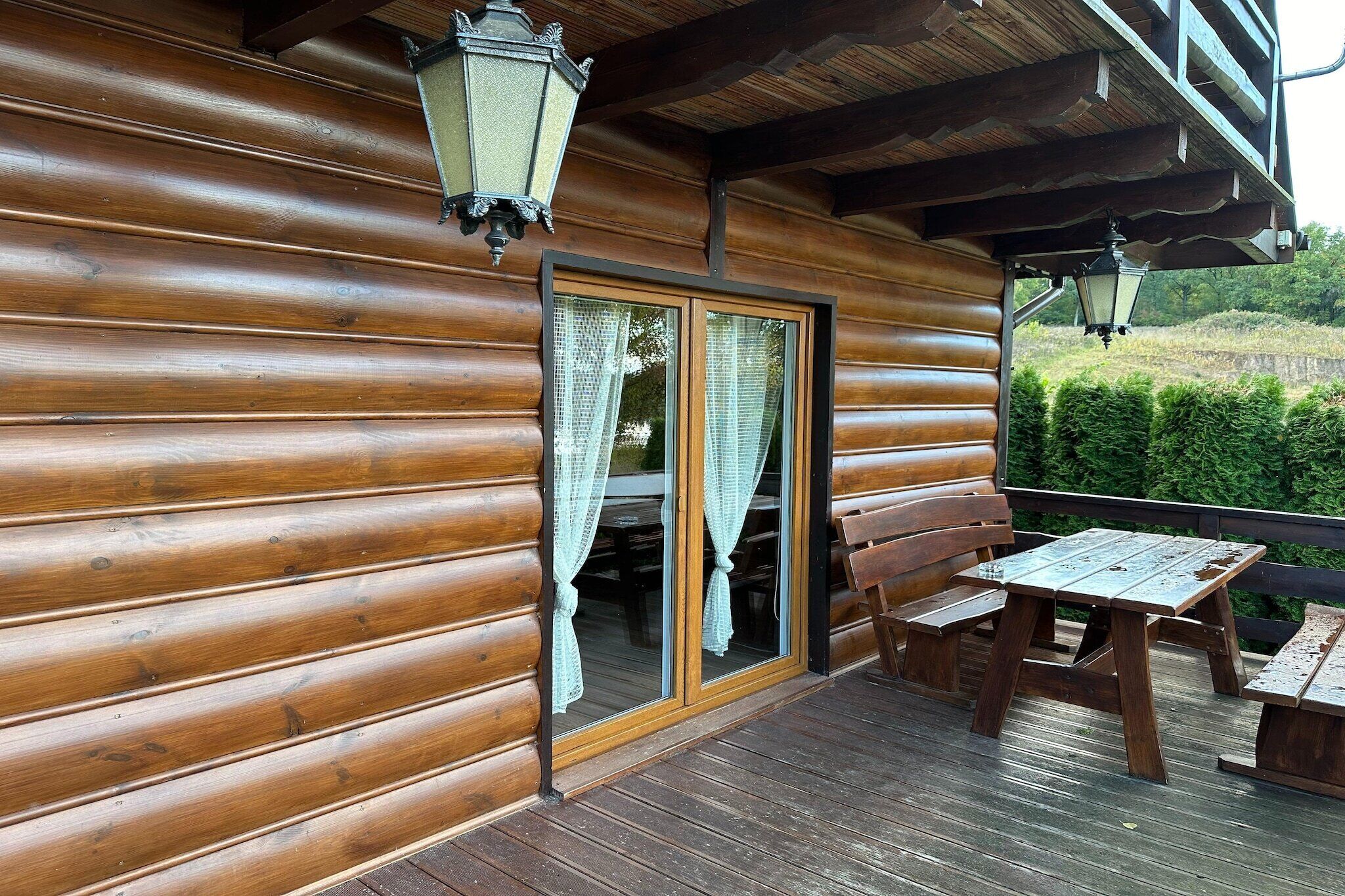 A wooden cabin with a wooden deck, a sliding glass door, and two benches.