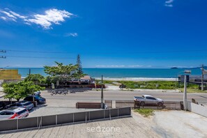 A coastal view with a parking area, a building with a sign, and a beach in the background.