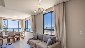 Un salon moderne avec un canapé, une table à manger et des chaises. De grandes fenêtres offrent une vue sur la mer.