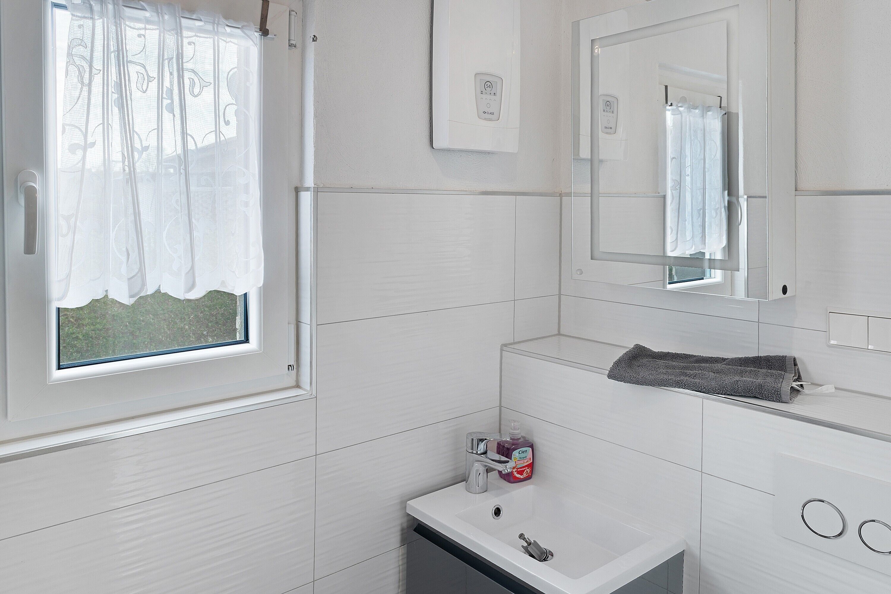 Une salle de bain avec une fenêtre, un miroir, un lavabo et un porte-serviettes.