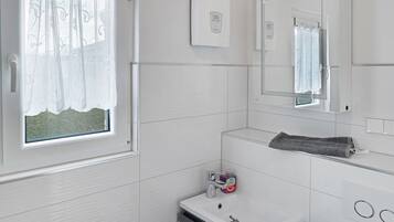 Une salle de bain avec une fenêtre, un miroir, un lavabo et un porte-serviettes.