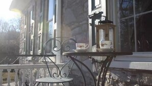 A stone building with a porch, a table with a cup and saucer, and a chair. - Stock's Manor Bed and Breakfast #1 (Mechanicsburg)