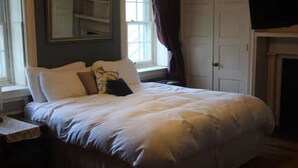 A neatly made bed with pillows, a bedside table, a window with curtains, and a door. - Stock's Manor Bed and Breakfast #1 (Mechanicsburg)