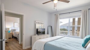 A bedroom with a bed, a TV, a dresser, a mirror, and a ceiling fan. - Ocean Club N303, Soundfront Condo in Indian Beach! (Indian Beach)