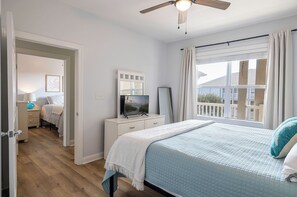Een slaapkamer met een bed, een televisie, een dressoir, een spiegel en een plafondventilator.