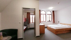 Una camera d'albergo con un letto singolo, una sedia, un tavolino e una finestra con tende.