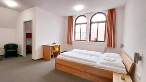 Una camera d'albergo con un letto, una scrivania, due sedie, un tavolino e una finestra con tende.