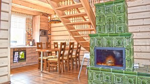 Un intérieur en bois comprenant un coin repas, un escalier et une cheminée recouverte de carreaux verts.