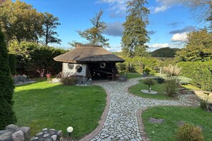 Un edificio rústico con techo de paja, rodeado de un jardín cuidado y un sendero de piedra que conduce a él.
