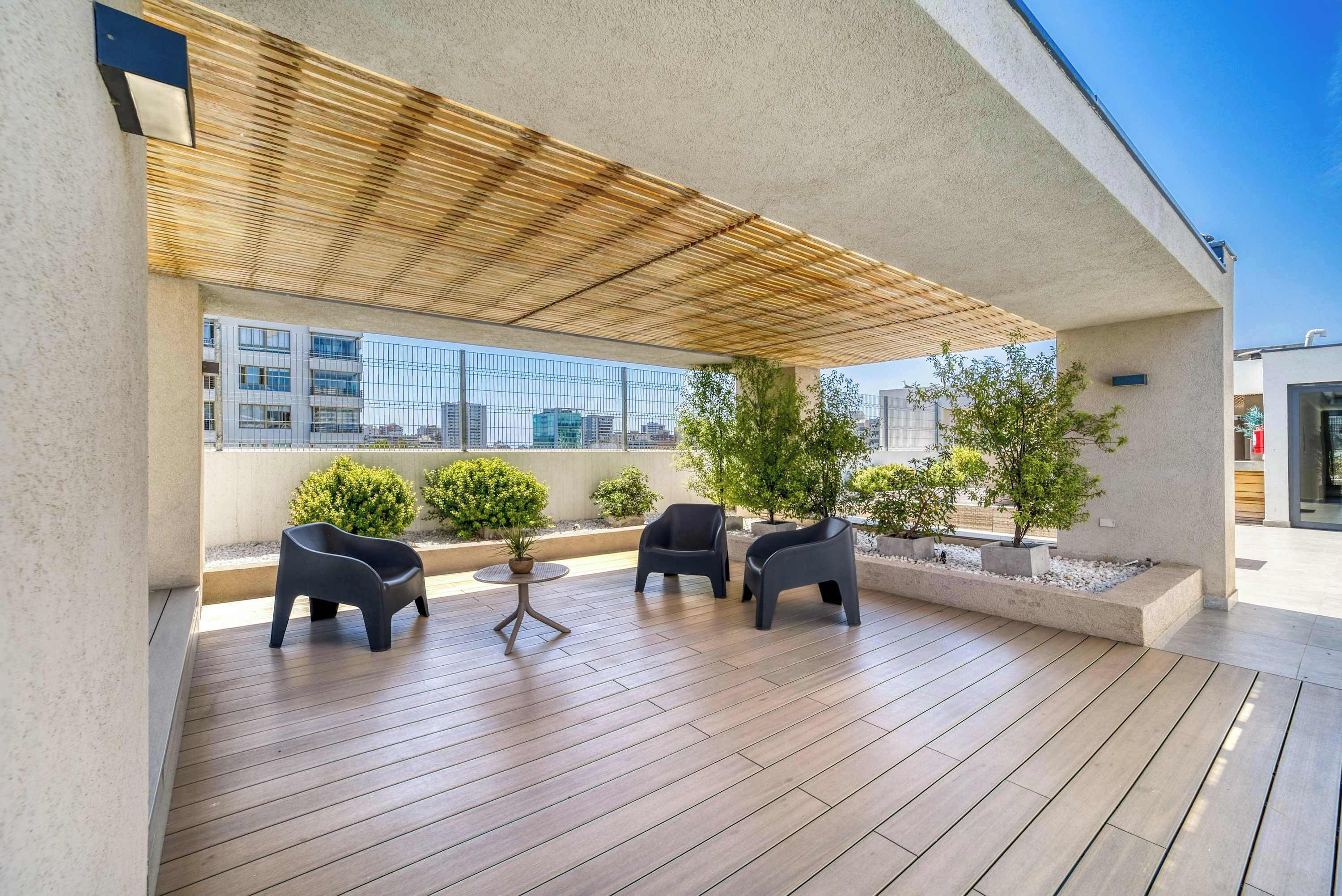 A covered outdoor seating area with wooden flooring, two black chairs, a small round table, and potted plants.