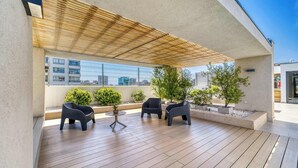 A covered outdoor seating area with wooden flooring, two black chairs, a small round table, and potted plants.