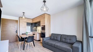 A modern kitchen with wooden cabinets, a dining table with chairs, and a grey sofa.
