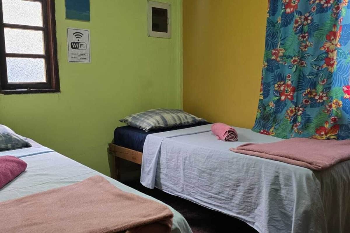 Une chambre avec deux lits, une fenêtre, un panneau indiquant la présence d’une connexion Wi-Fi et un rideau à motifs floraux.