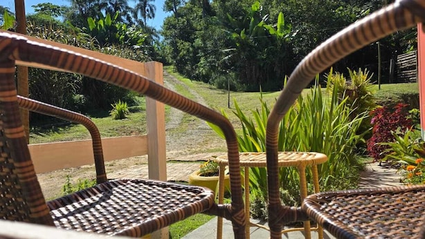 Wicker chairs and a small round table in a garden area with a view of a grassy path and greenery. - O BREJO ENCANTADO HOSTEL E HOSPEDAGEM  (Embu das Artes)