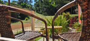 Wicker chairs and a small round table in a garden area with a view of a grassy path and greenery. - O BREJO ENCANTADO HOSTEL E HOSPEDAGEM  (Embu das Artes)