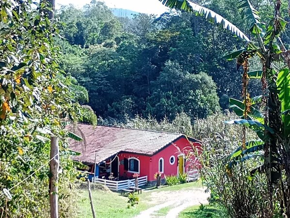 Un edificio rojo con tejado de tejas, rodeado de abundante vegetación y un sendero de tierra que conduce a él.