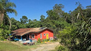 A red building with a tiled roof, surrounded by greenery and trees. - O BREJO ENCANTADO HOSTEL E HOSPEDAGEM  (Embu das Artes)