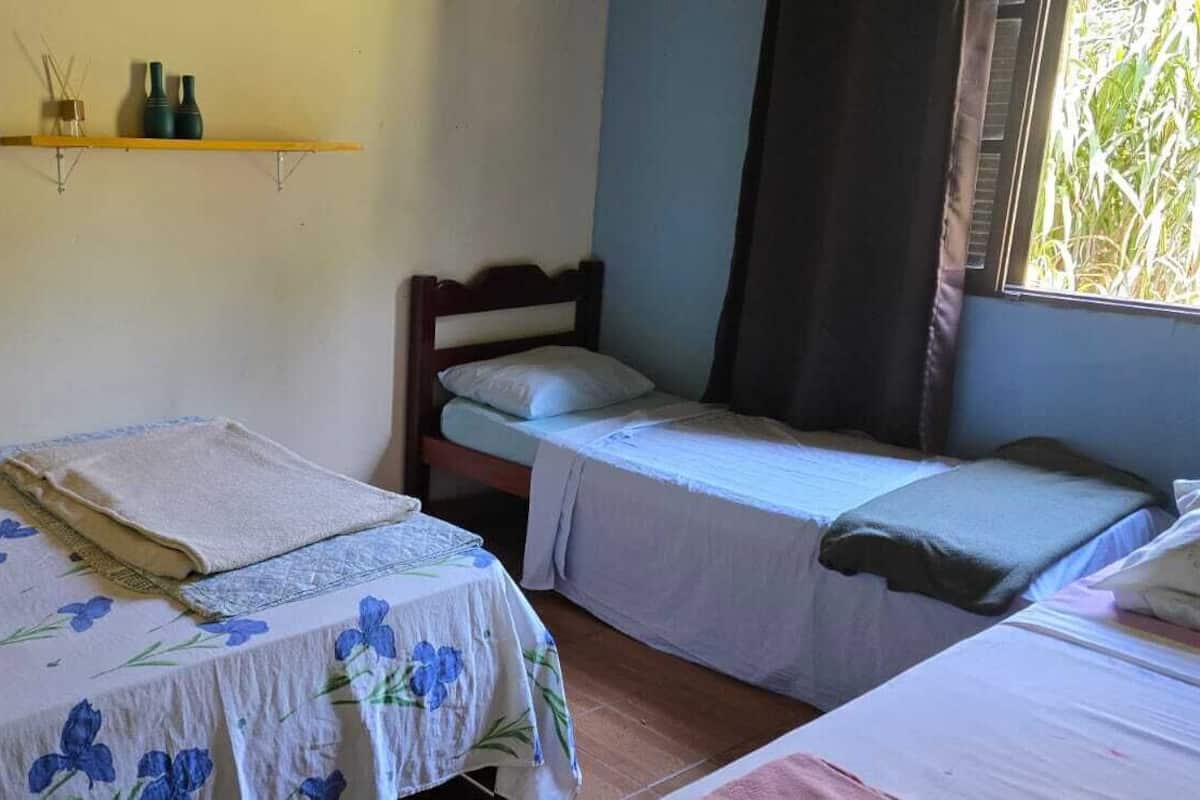Une chambre avec deux lits, une tête de lit en bois, une fenêtre avec des rideaux et une étagère ornée d’objets décoratifs.