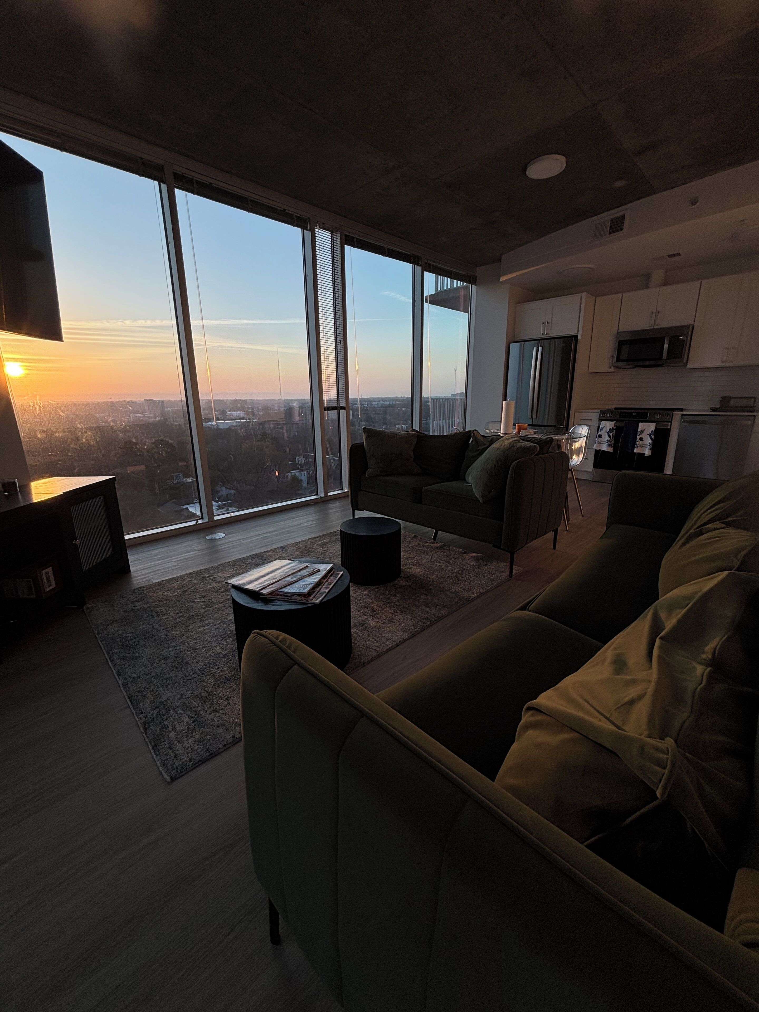 A modern living room with a large window, a sofa, a coffee table, and a kitchen area.