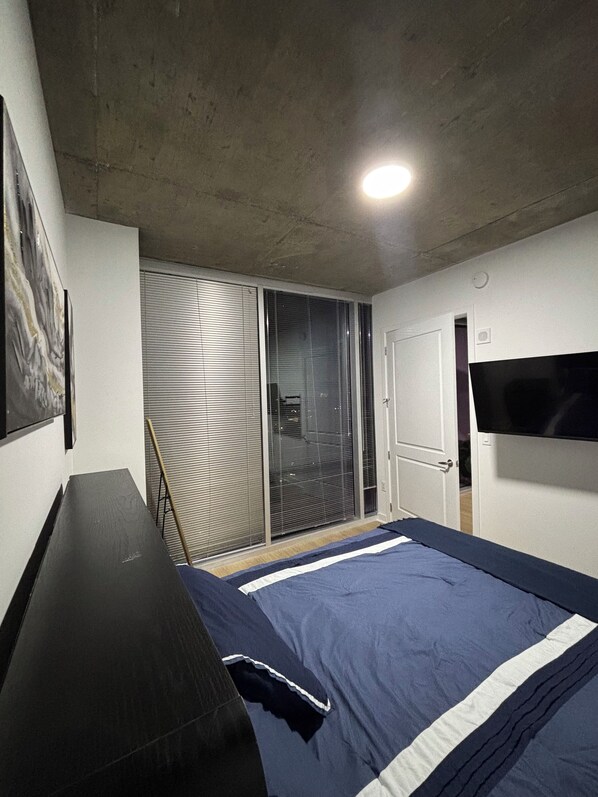 Une chambre à coucher avec un lit, une télévision, une porte et une fenêtre avec des stores.