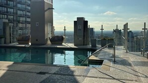 Une piscine située sur le toit, offrant une vue sur les gratte-ciel de la ville, les bâtiments modernes et un ciel dégagé.