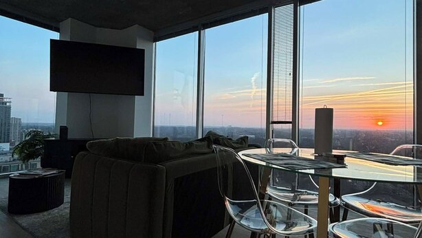 Un salon moderne avec une table à manger en verre, un canapé en cuir et de grandes fenêtres donnant sur la ville.