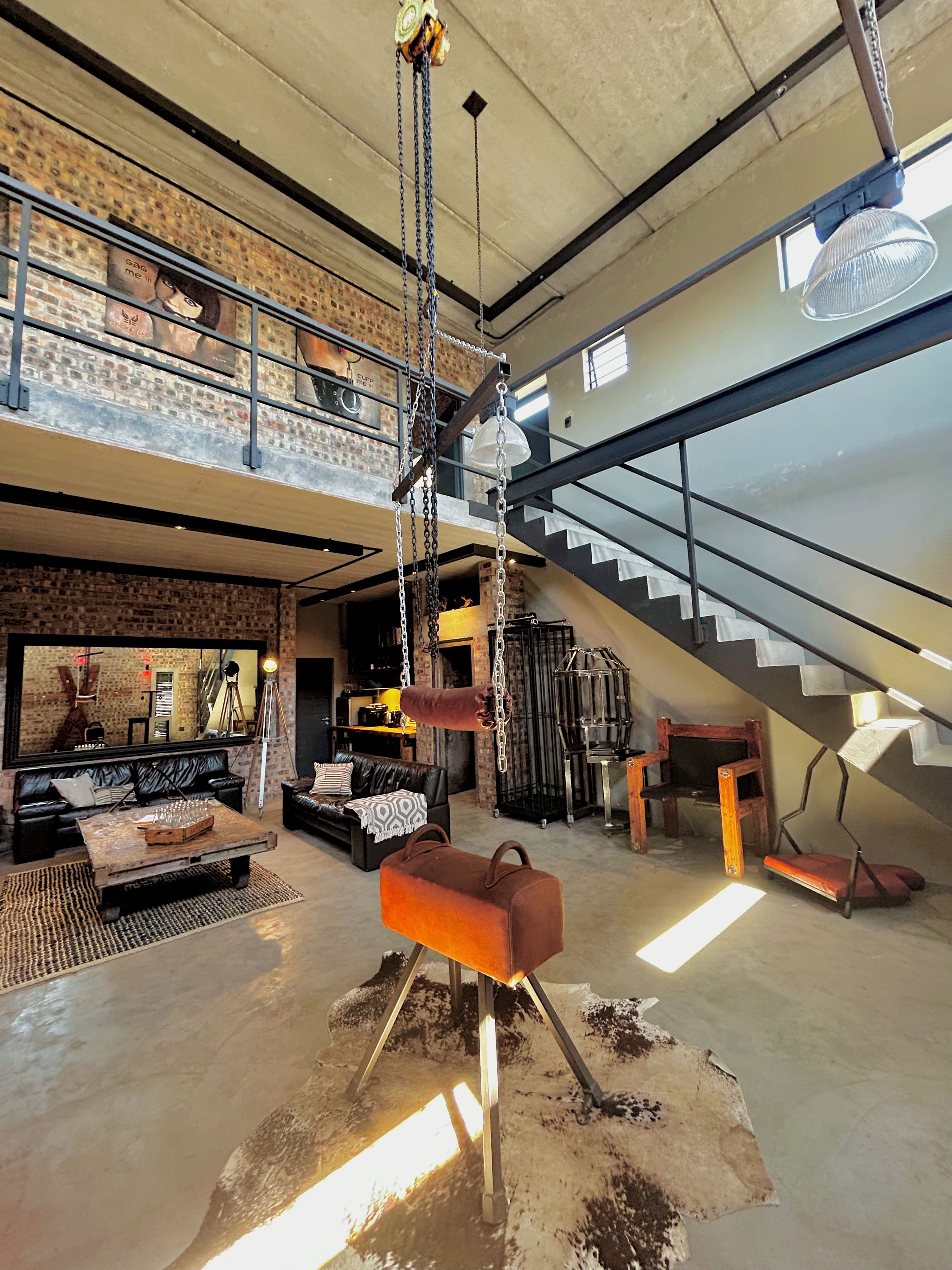 A spacious loft with a high ceiling, exposed brick walls, a mezzanine level, and a staircase.