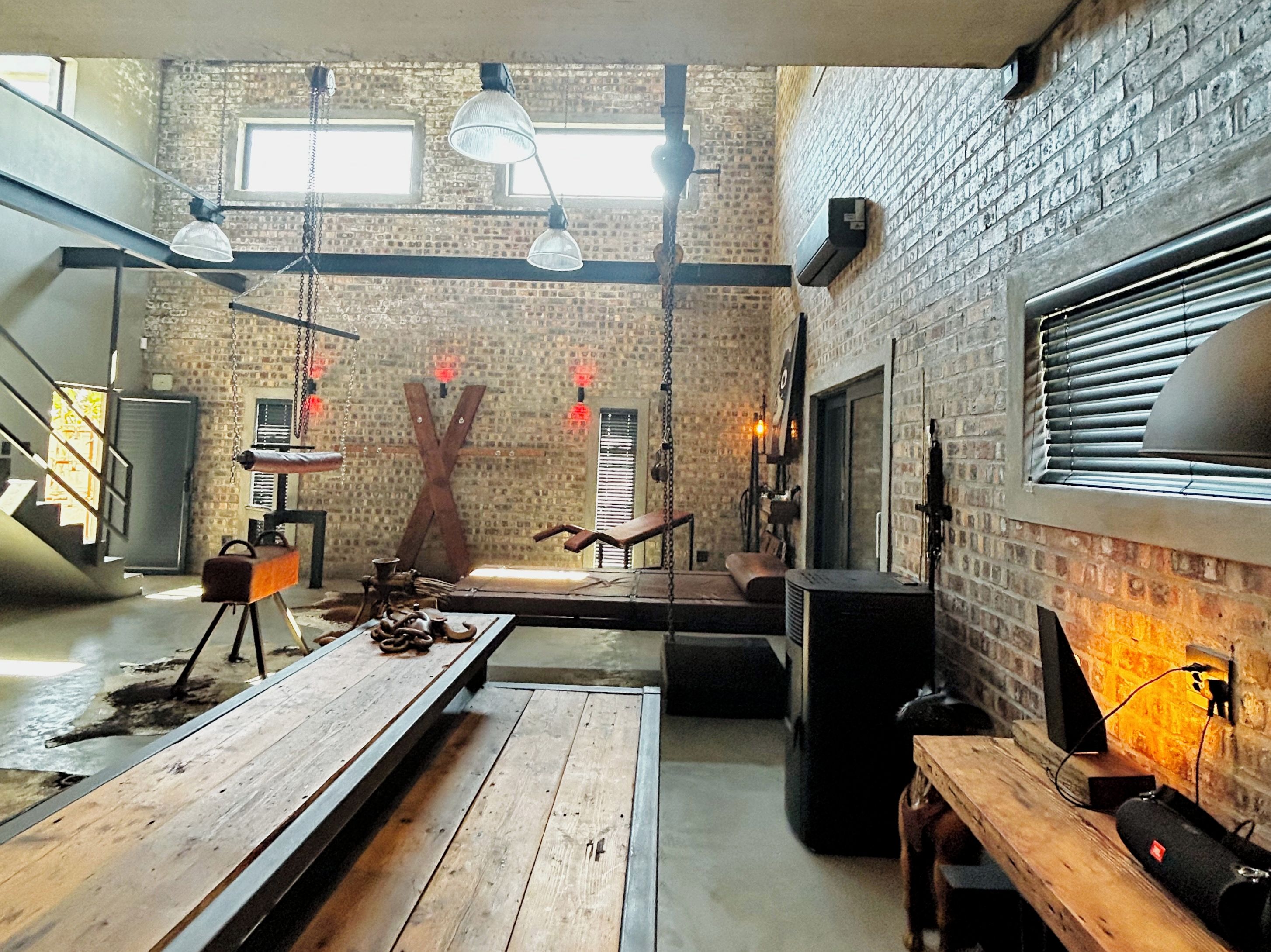 A spacious loft with exposed brick walls, a loft bed, a wooden dining table, and a large window with blinds.