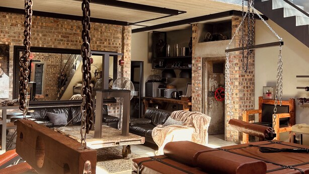 Un loft espacioso con techo alto, paredes de ladrillo visto, una cama de altillo, una hamaca y una zona de cocina.