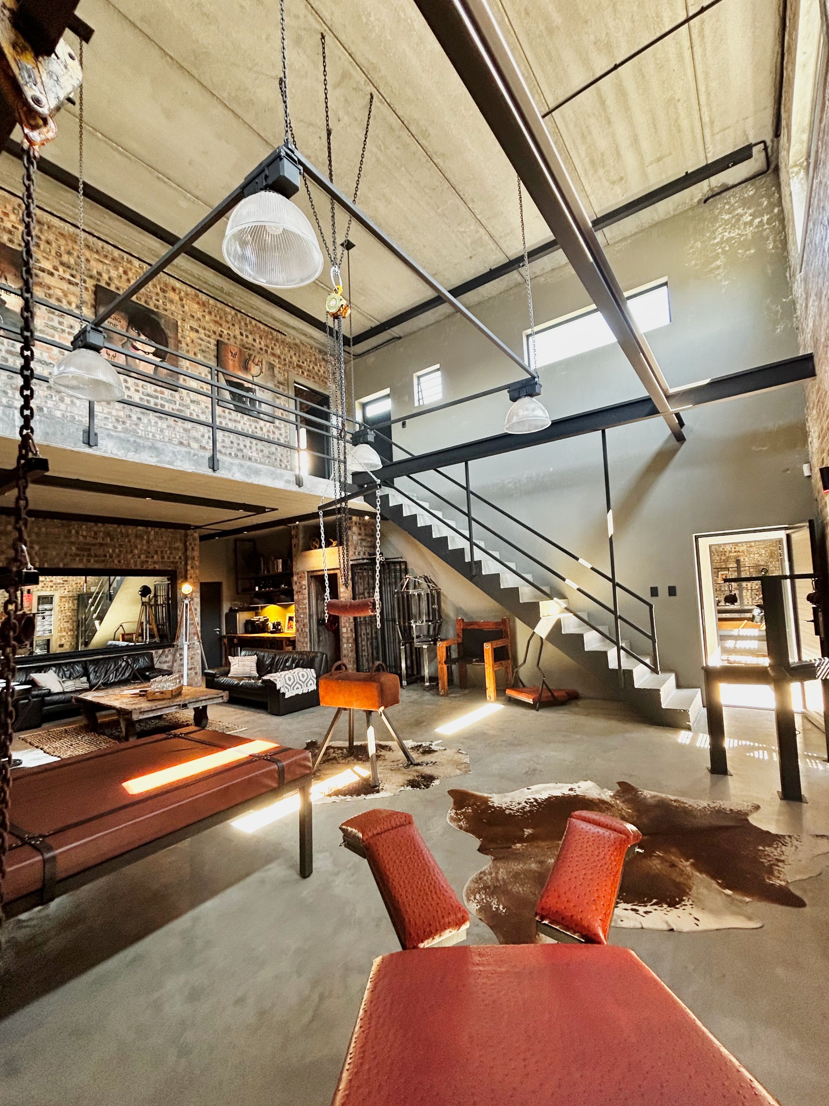 Un loft espacioso con techo alto, paredes de ladrillo visto y un entrepiso, además de una escalera.