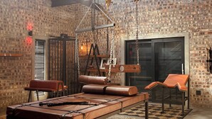 Un loft espacioso con paredes de ladrillo visto, una cama grande con estructura metálica y una silla colgante tipo hamaca.