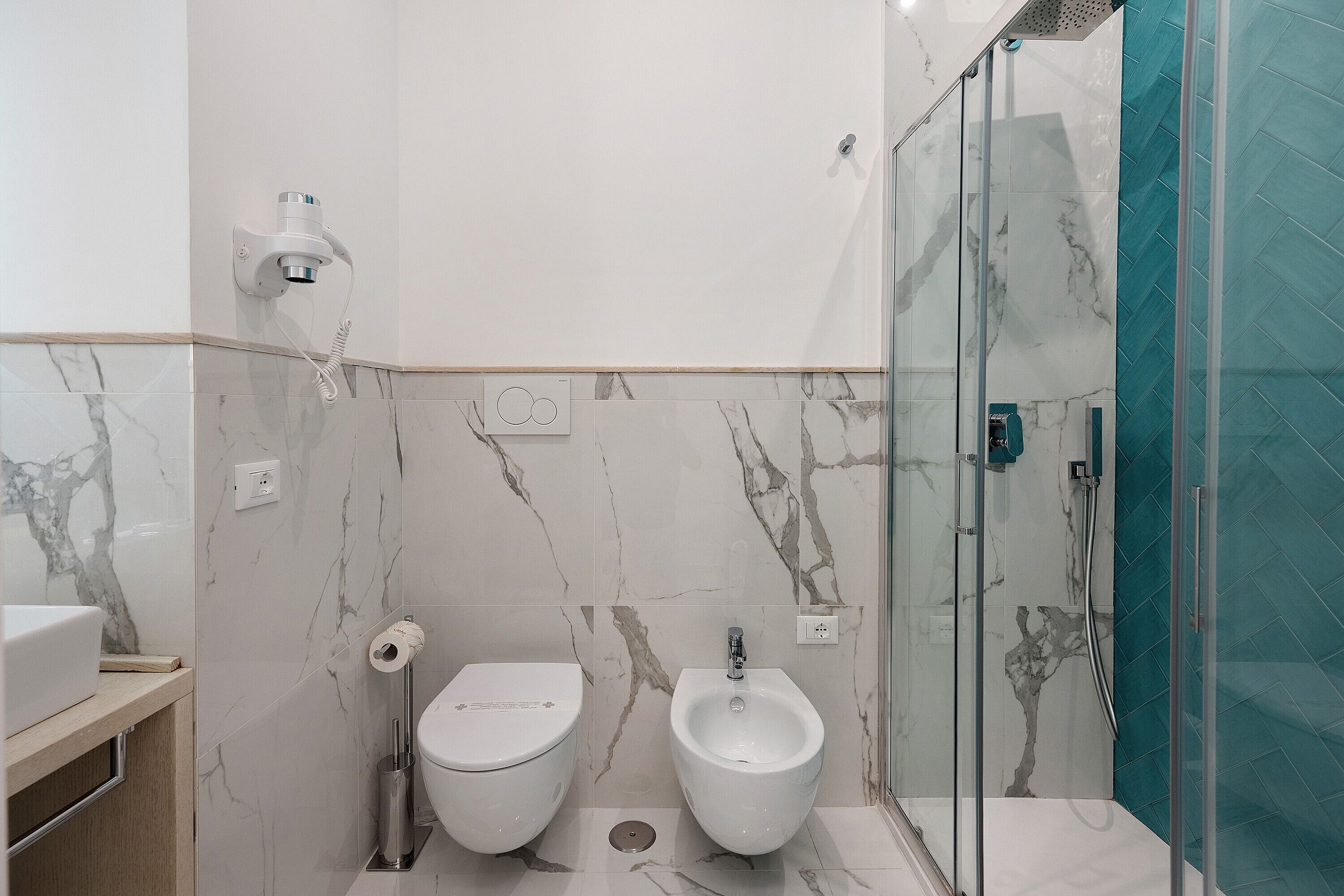 Un baño moderno con bidé, inodoro y ducha con mampara de vidrio.