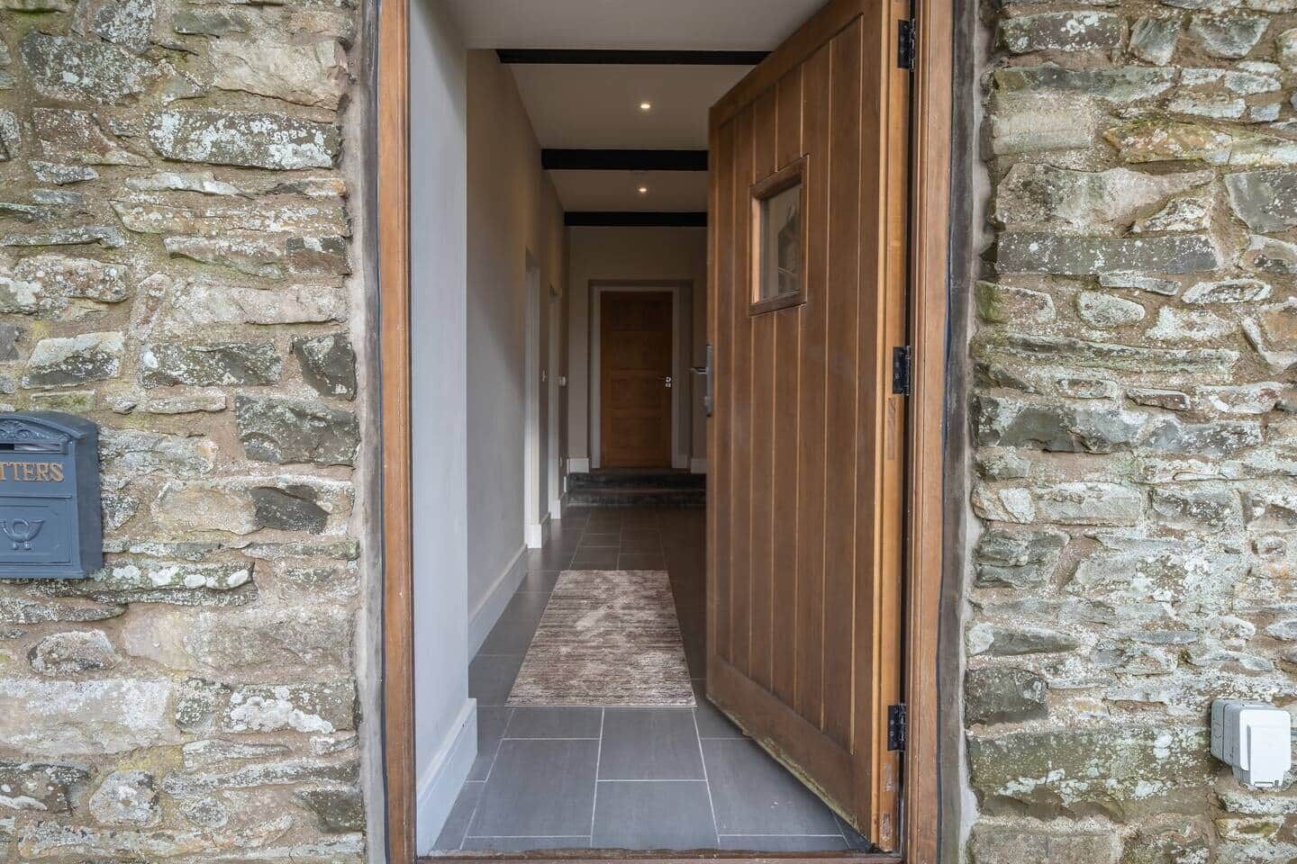 A stone-walled hallway with a wooden door and a mailbox.