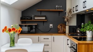 Una cocina moderna con armarios blancos, encimera de madera, horno empotrado y comedor con mesa y sillas blancas.