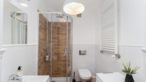 Un baño con ducha de vidrio, un lavabo blanco, inodoro y un florero con flores en la encimera.