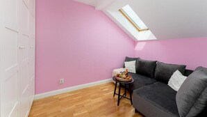 Una habitación con pared rosa, un sofá negro, una pequeña mesa con fruta y un tragaluz.
