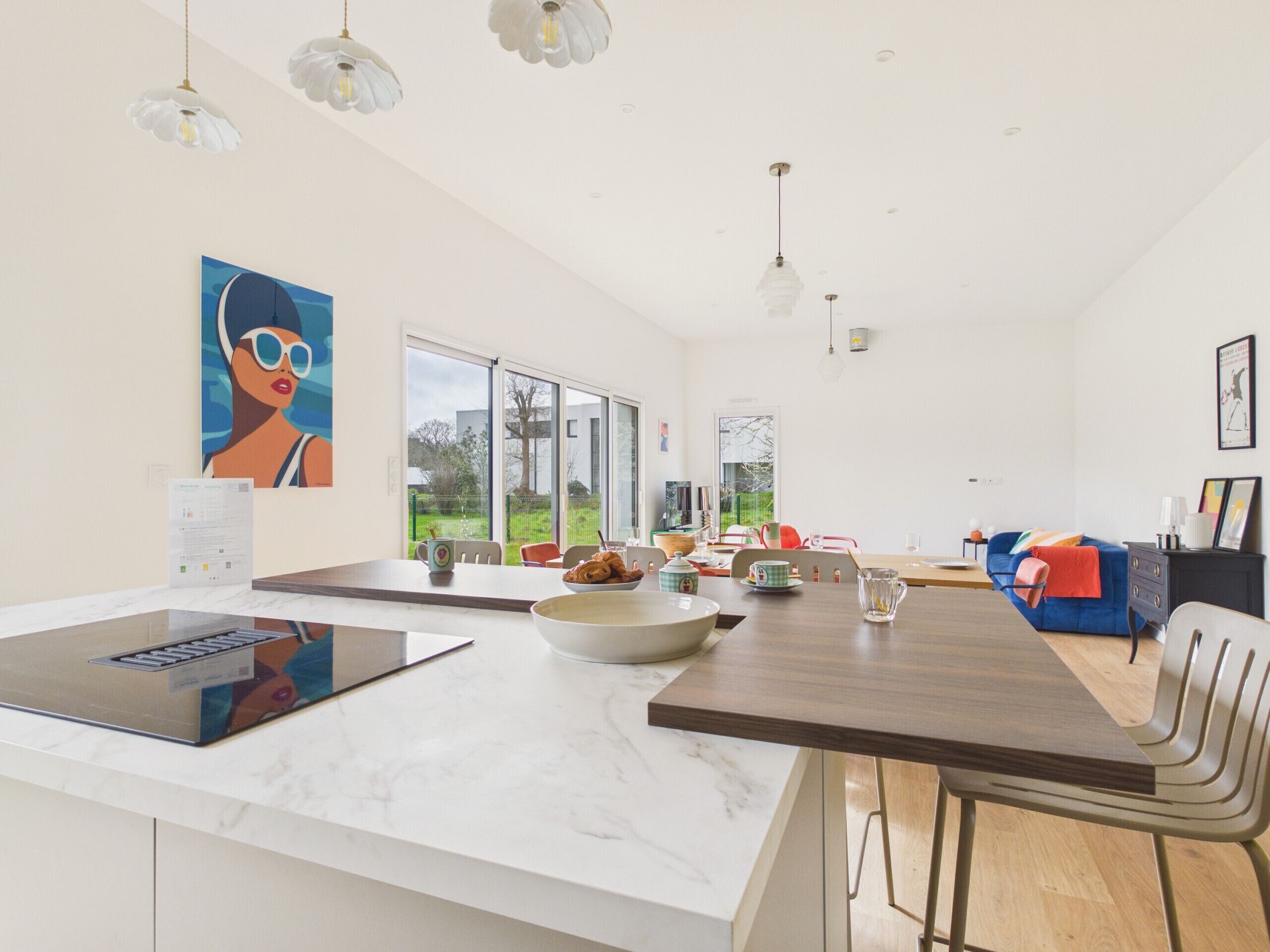 A modern kitchen with a large island, a dining area with a long table, and a living space with a sofa and chairs.