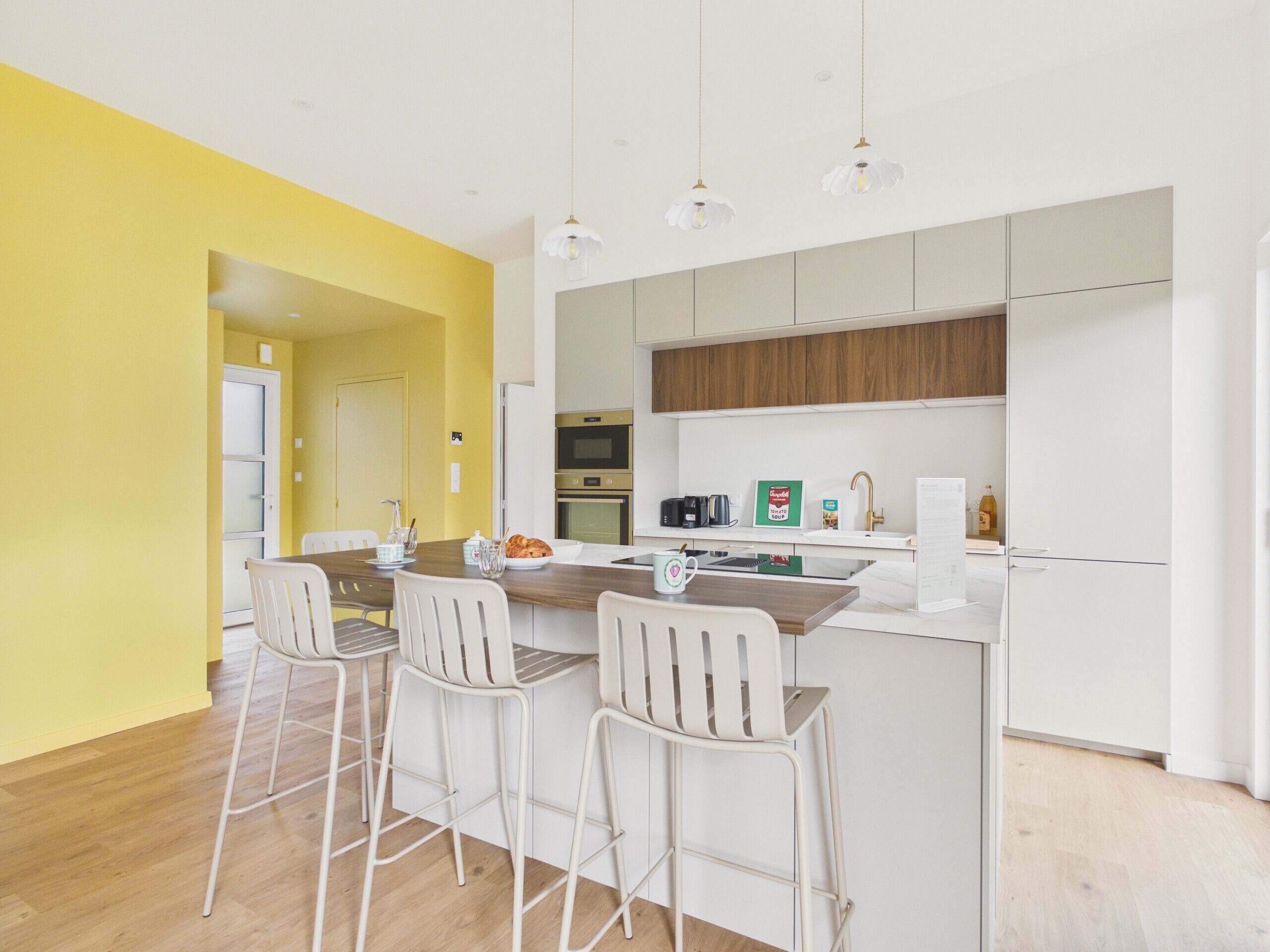 Una cocina moderna con una isla central, taburetes blancos y una pared de acento amarilla.