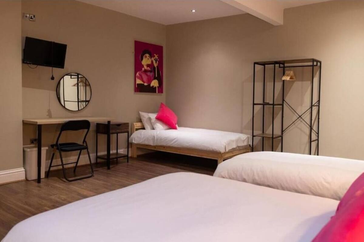 Quarto com duas camas, uma escrivaninha, uma cadeira, uma televisão e um espelho.